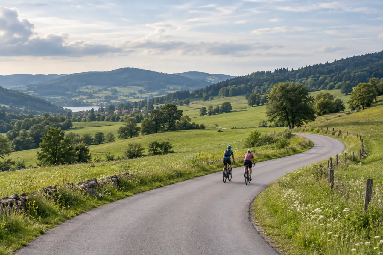 Two cyclists riding a winding country road through green hills